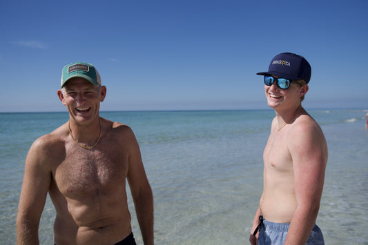 Two friends laughing on the beach, one in a Sarasota cap