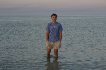 Young man in a Sarasota tee standing in the calm Gulf at dusk