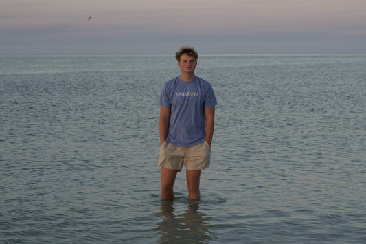 Young man in a Sarasota tee standing in the calm Gulf at dusk