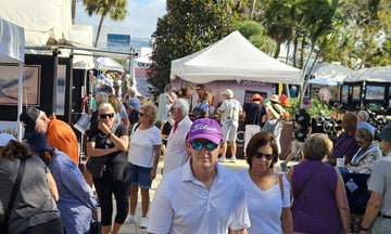 Crowds walking between white artist tents under the palms at an art festival on St. Armands Circle