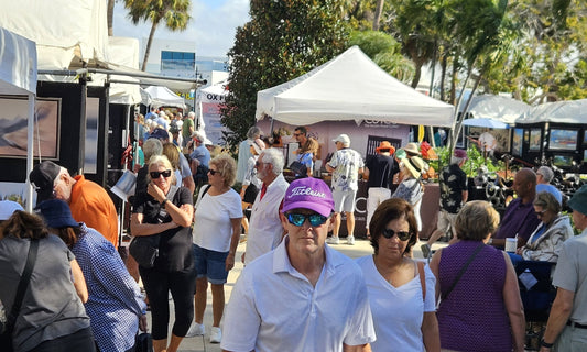 Crowds walking between white artist tents under the palms at an art festival on St. Armands Circle