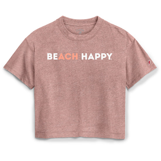 A heathered dusty rose short-sleeve crop top featuring the text 'BEACH HAPPY' printed across the chest, with 'BEACH' in white and 'HAPPY' in a coral-orange color. A small red and white logo is visible on the right sleeve.
