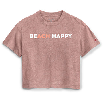 A heathered dusty rose short-sleeve crop top featuring the text 'BEACH HAPPY' printed across the chest, with 'BEACH' in white and 'HAPPY' in a coral-orange color. A small red and white logo is visible on the right sleeve.